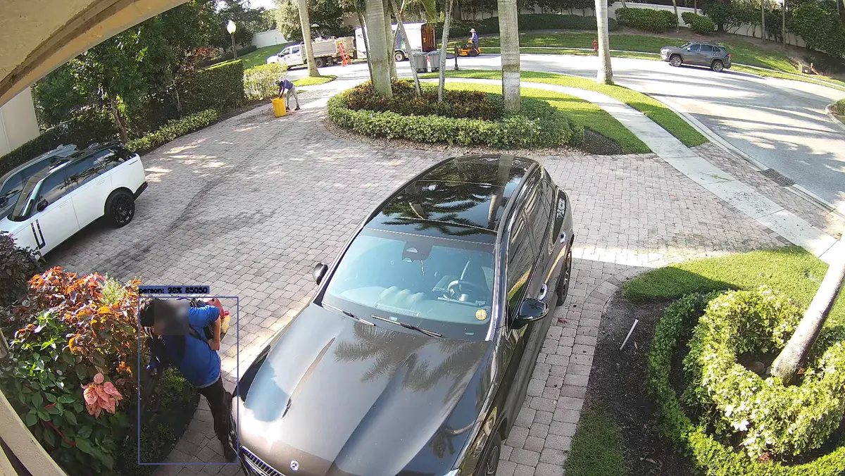 Driveway snapshot of a landscaper working near the hedge with the crew's truck and mower visible in the background